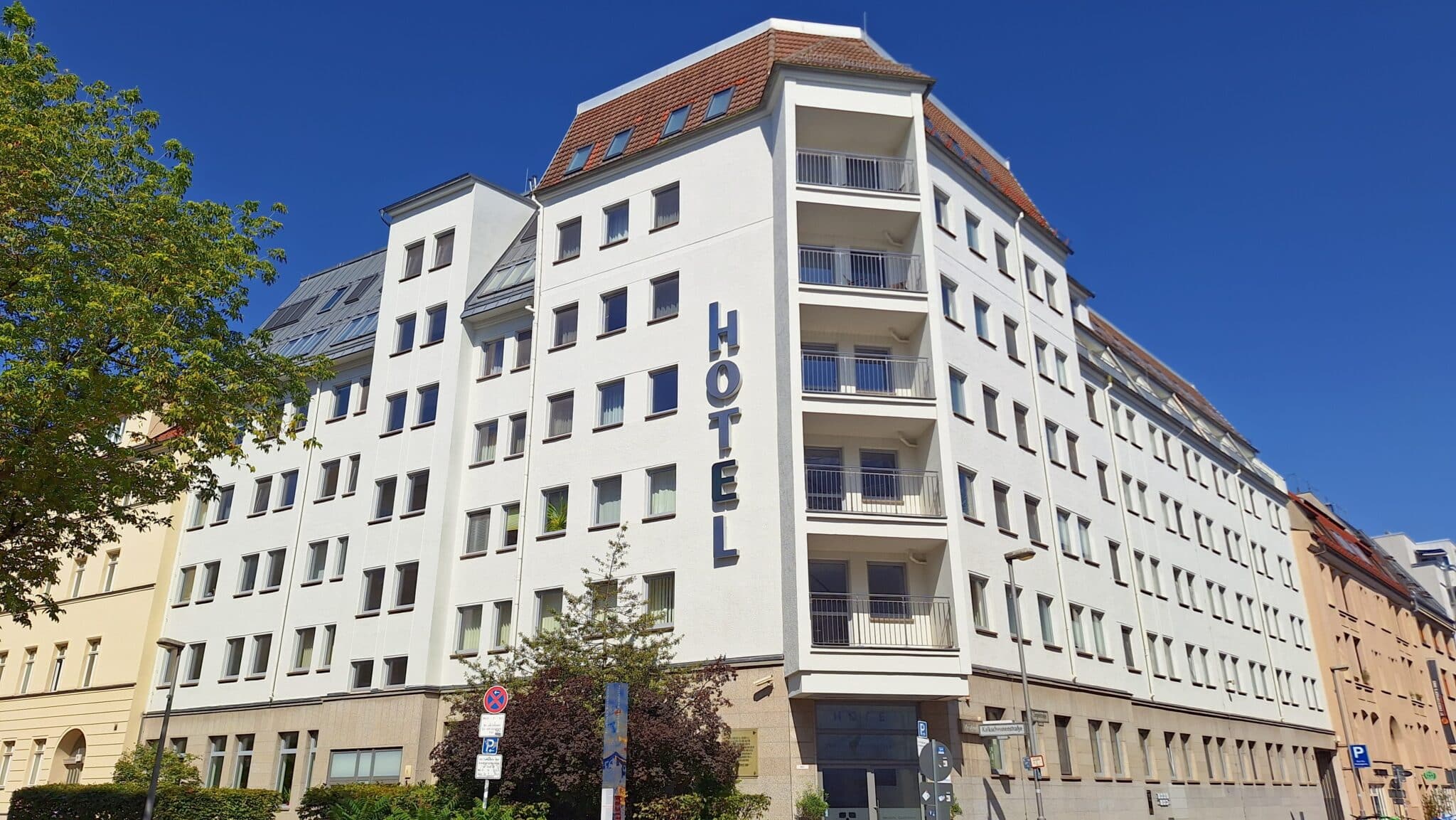 Weißes Hotelgebäude mit fünf Stockwerken und großen Fenstern in einer städtischen Umgebung.