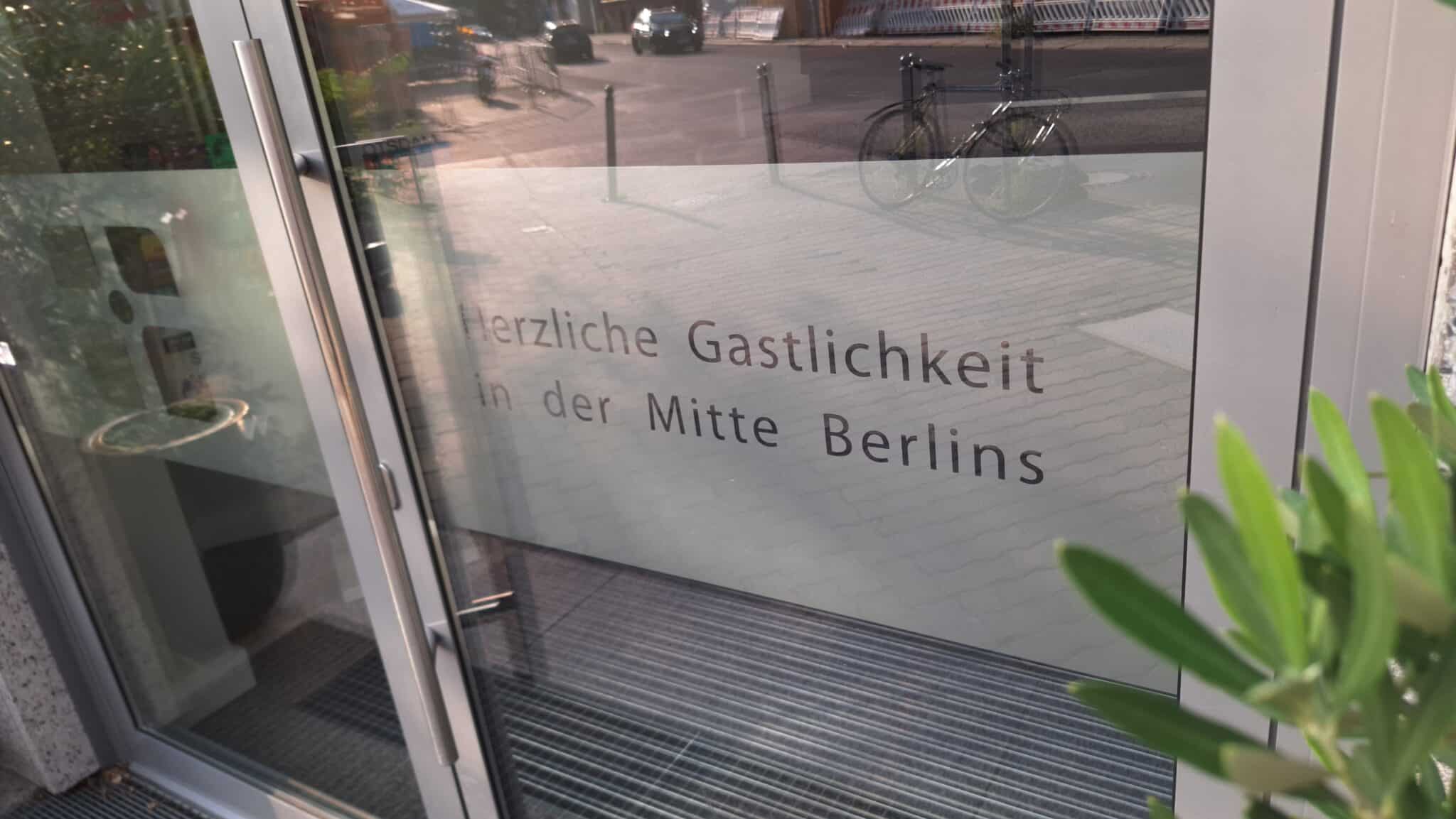 Eingangstür mit dem Schriftzug 'Herzliche Gastlichkeit in der Mitte Berlins' auf einer Glasfläche.