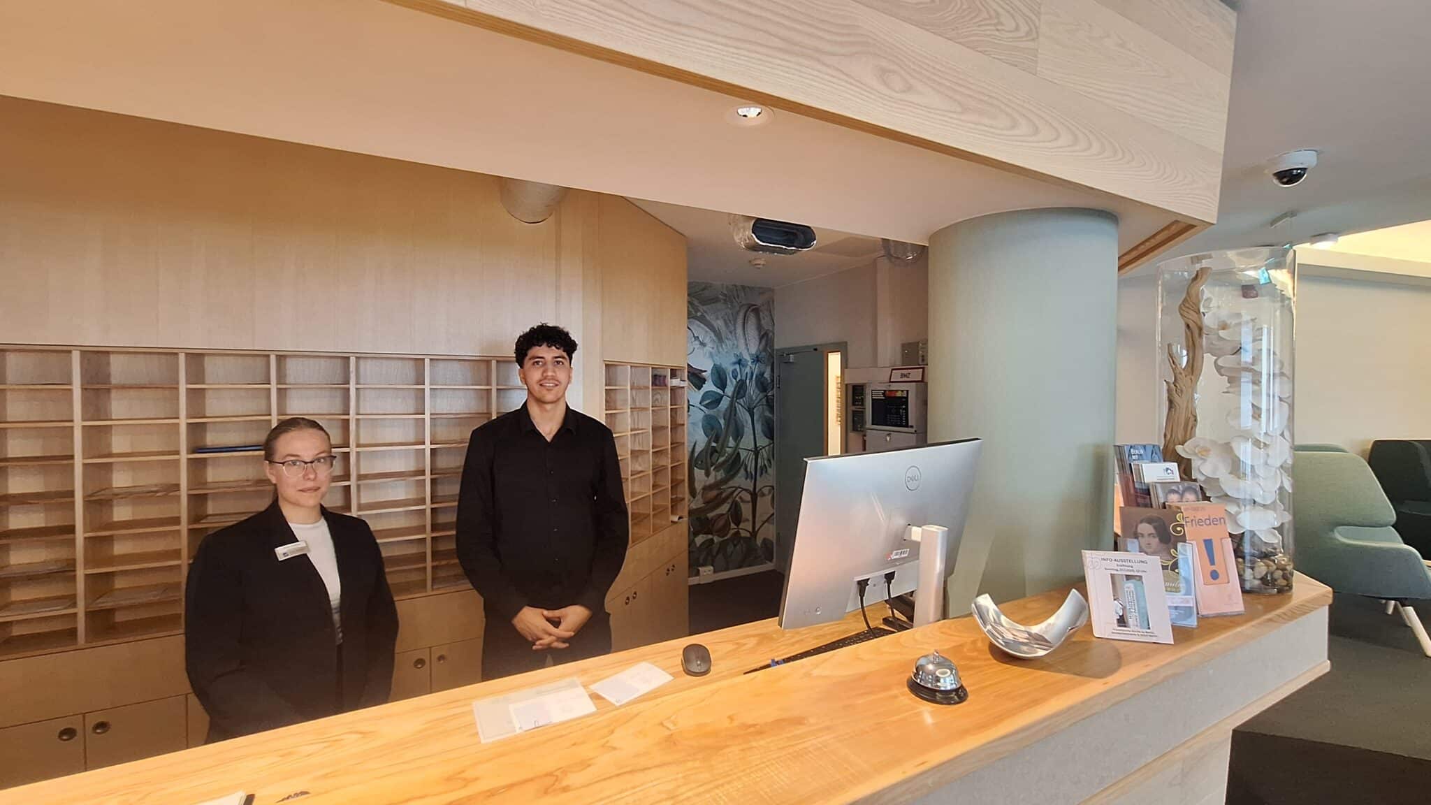 Rezeption mit zwei Mitarbeitern in einem modernen Empfangsbereich des Hotel Dietrich Bonhoeffer Haus.