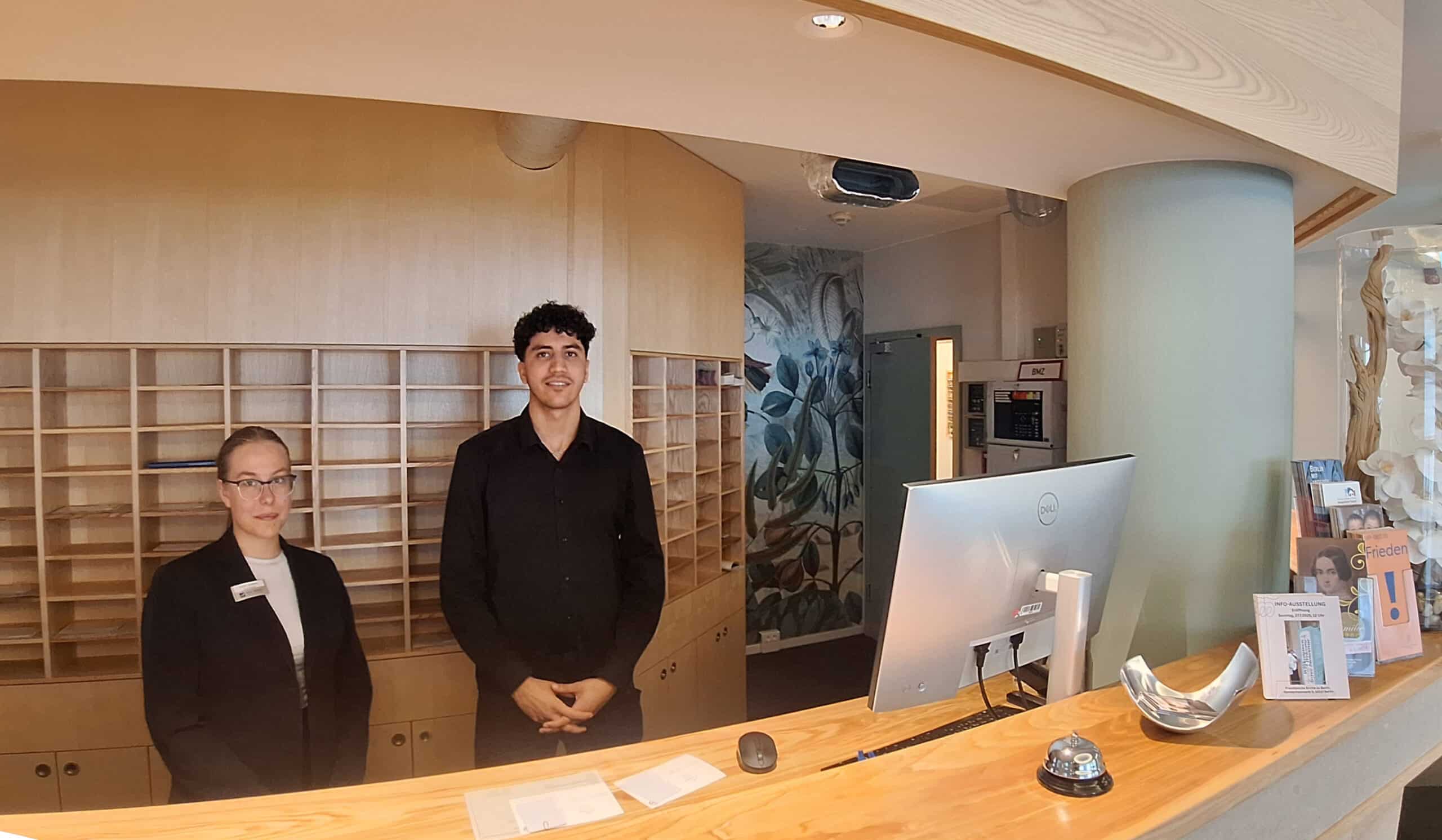 Rezeption mit zwei Mitarbeitern in einem modernen Foyer des Hotel Dietrich Bonhoeffer Haus.