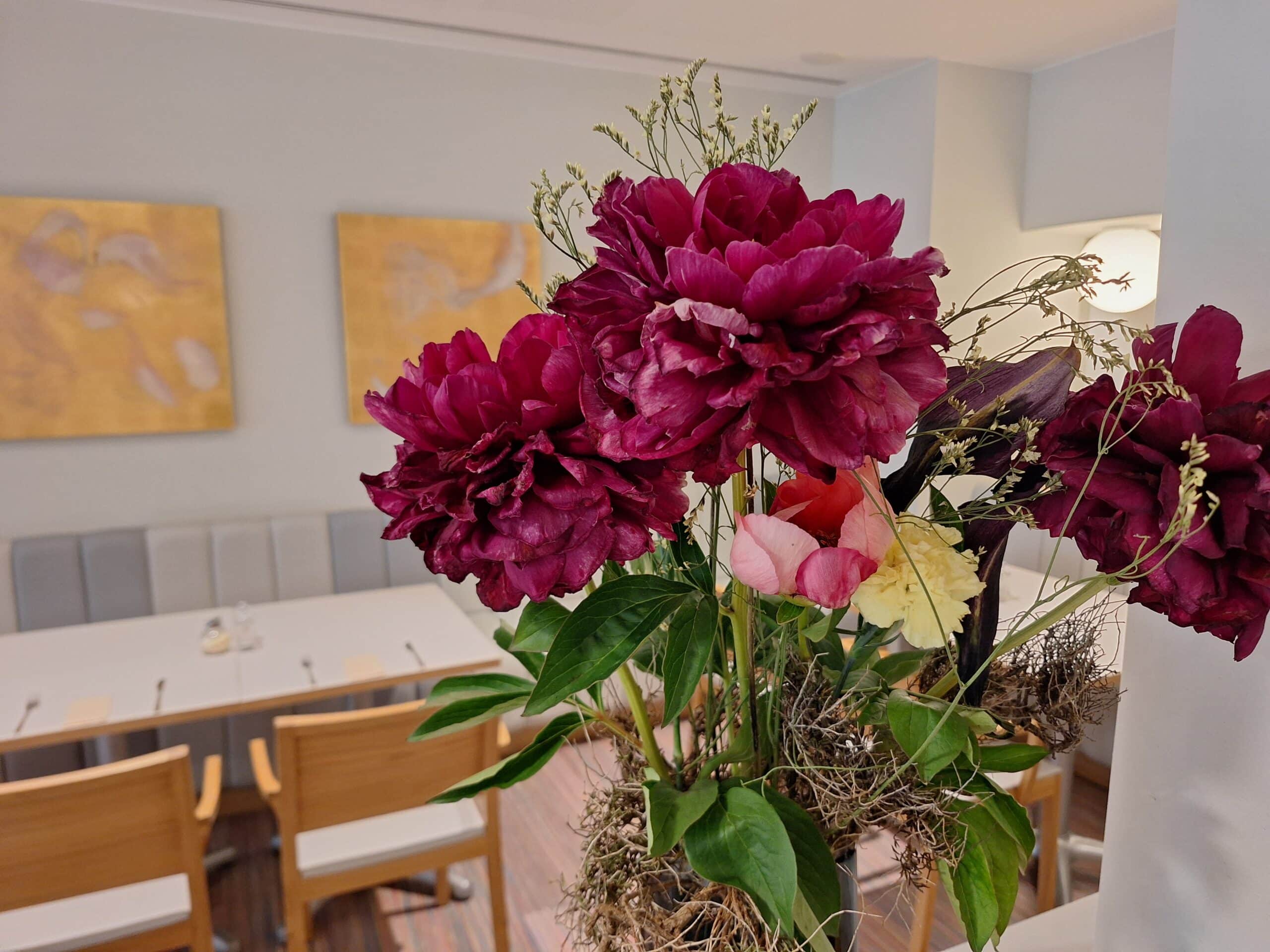 Ein Arrangement aus roten und rosa Blumen in einer Vase, platziert in einem Restaurant mit einem modernen Interieur.