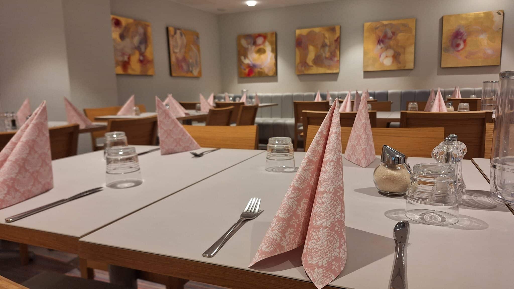 Elegante Restauranttische mit rosa Servietten und Gläsern in einem modernen Innenraum.