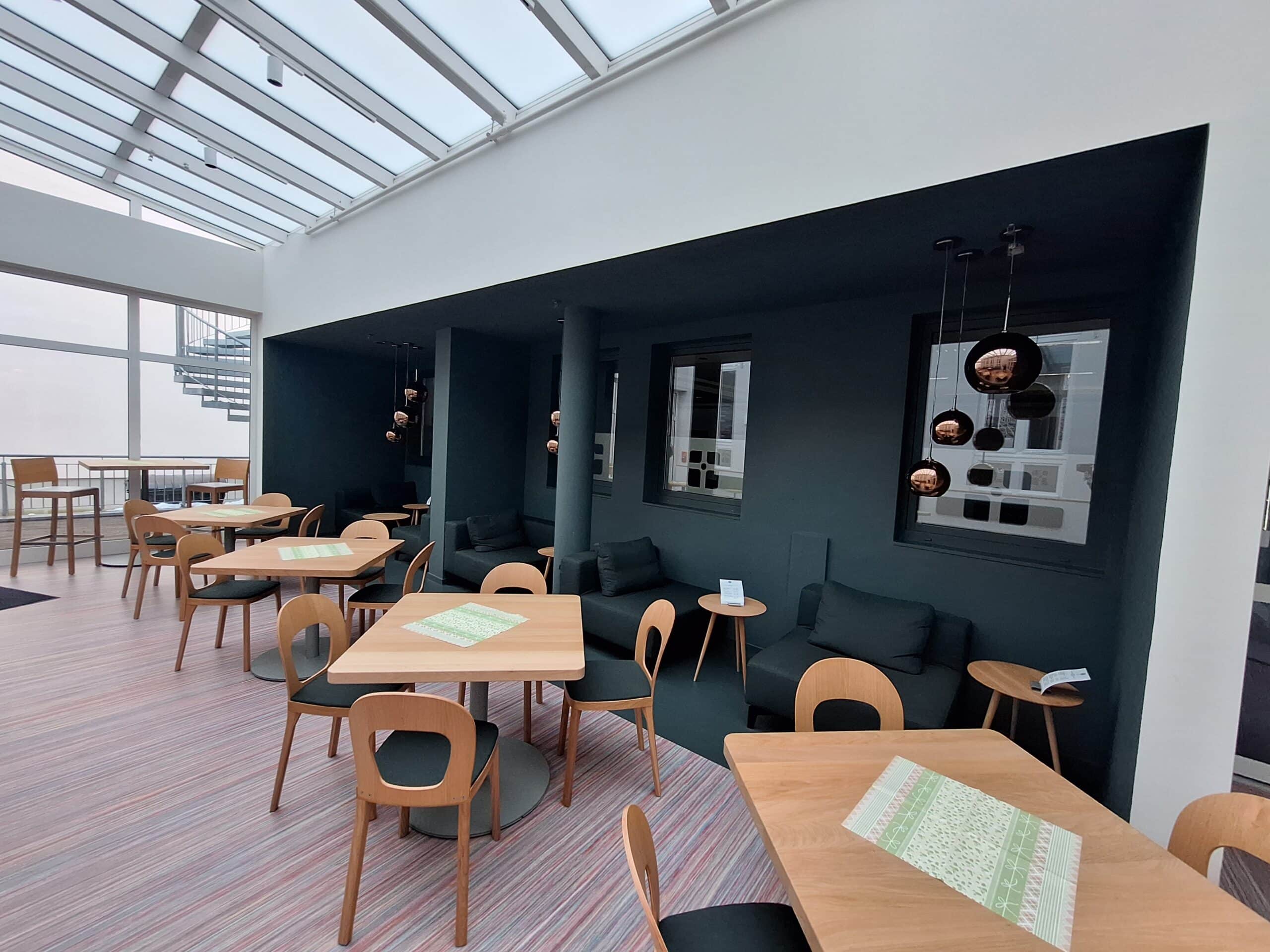 Moderne Sitzbereiche mit Holztischen und bequemen Stühlen in einem hellen Raum mit großen Fenstern.