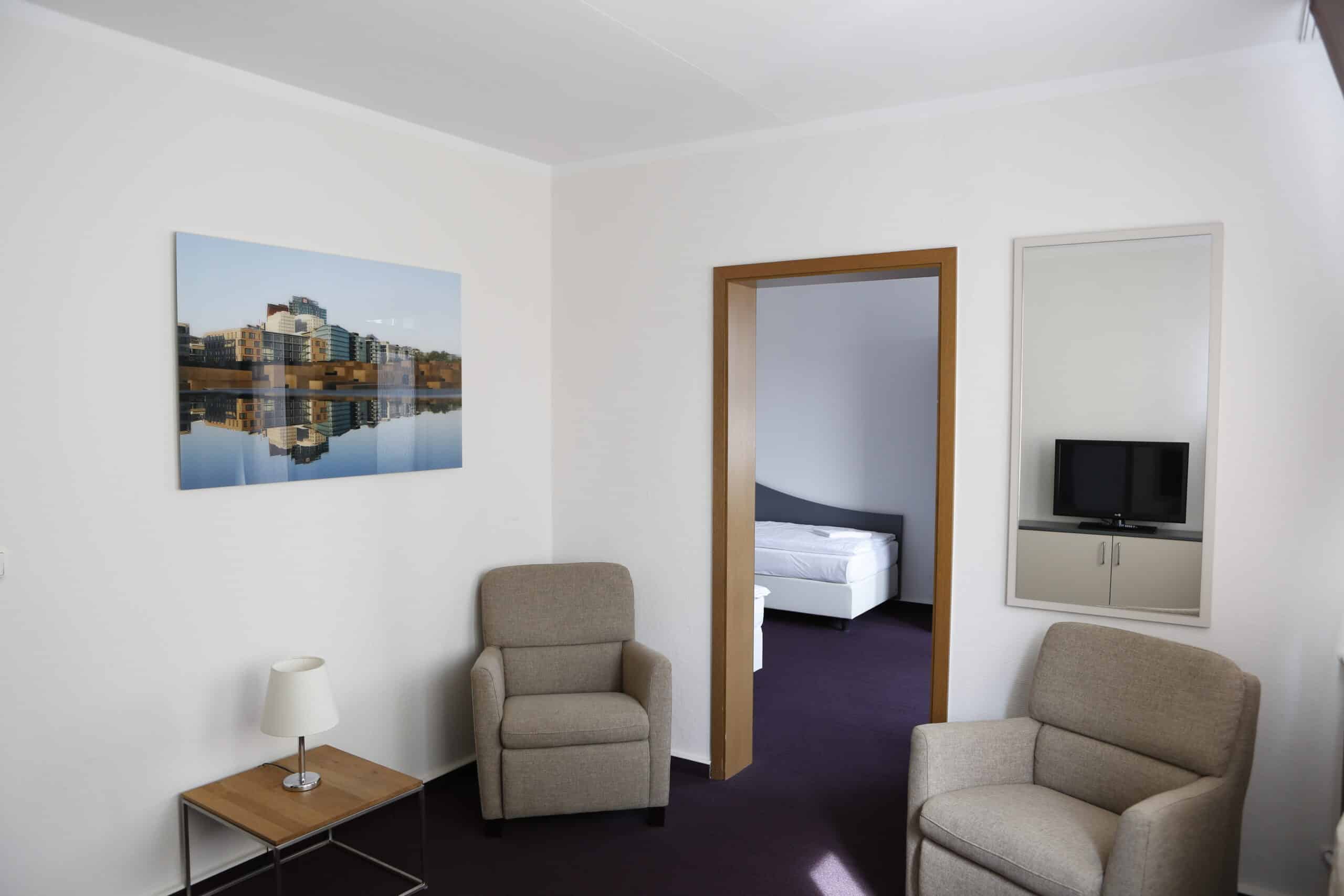 Ein Hotelzimmer im Dietrich Bonhoeffer Haus mit zwei beigen Sesseln und einem Tisch.