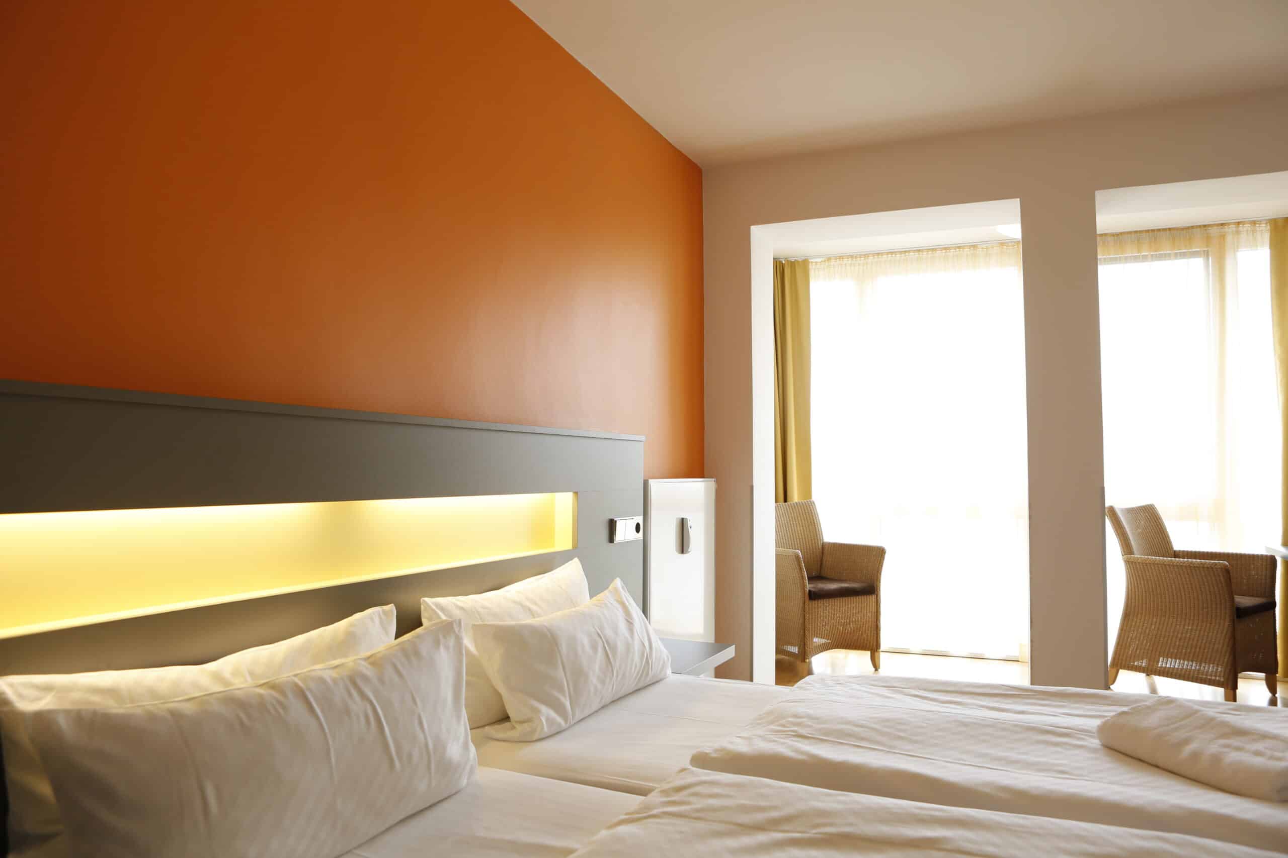 Zimmer mit zwei Einzelbetten und orangefarbener Wand, ausgestattet mit einem Tisch und Stühlen.