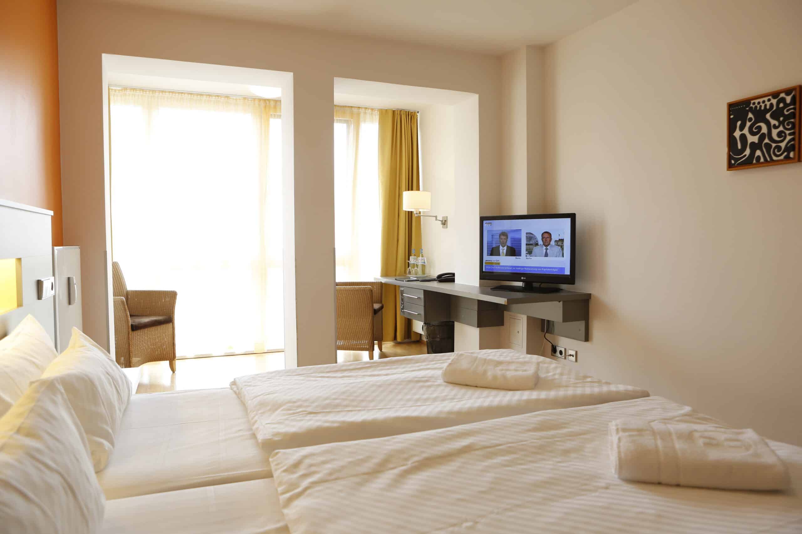 Ein Doppelzimmer mit zwei Betten, einem Fernseher und einem Schreibtisch im Hotel Dietrich Bonhoeffer Haus.