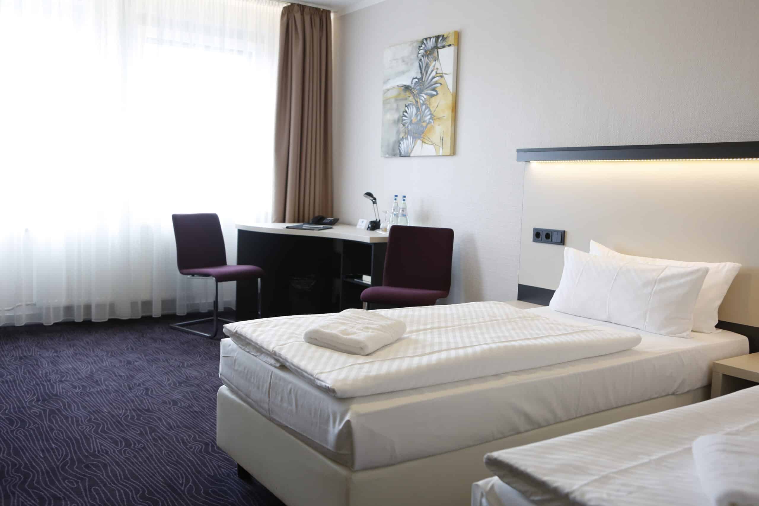 Zimmer im Hotel Dietrich Bonhoeffer Haus mit zwei Betten, Schreibtisch und Fenster.