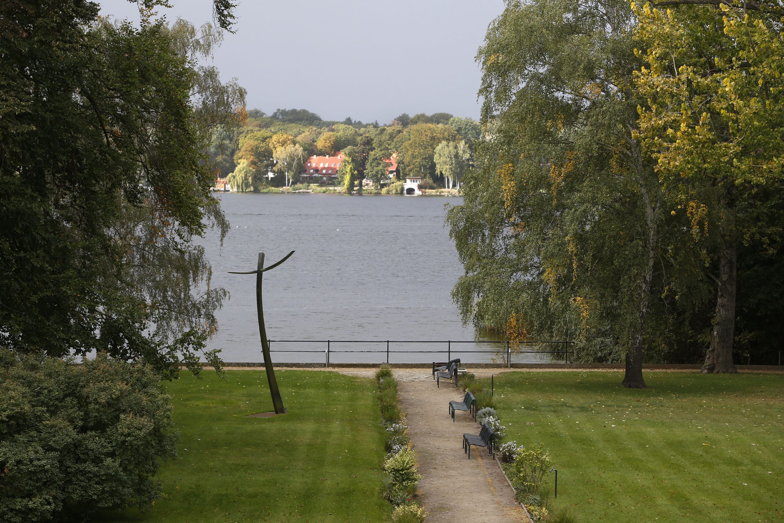 Skulptur in einem Garten mit Blick auf einen See und Bäume im Hintergrund.
