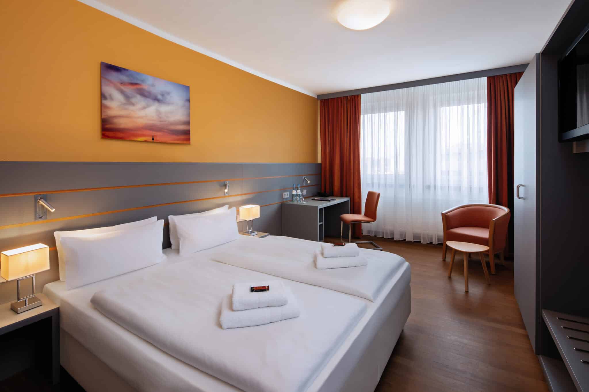 Doppelzimmer mit zwei Betten, einem Schreibtisch und einem Stuhl in einem modernen Hotelzimmer.