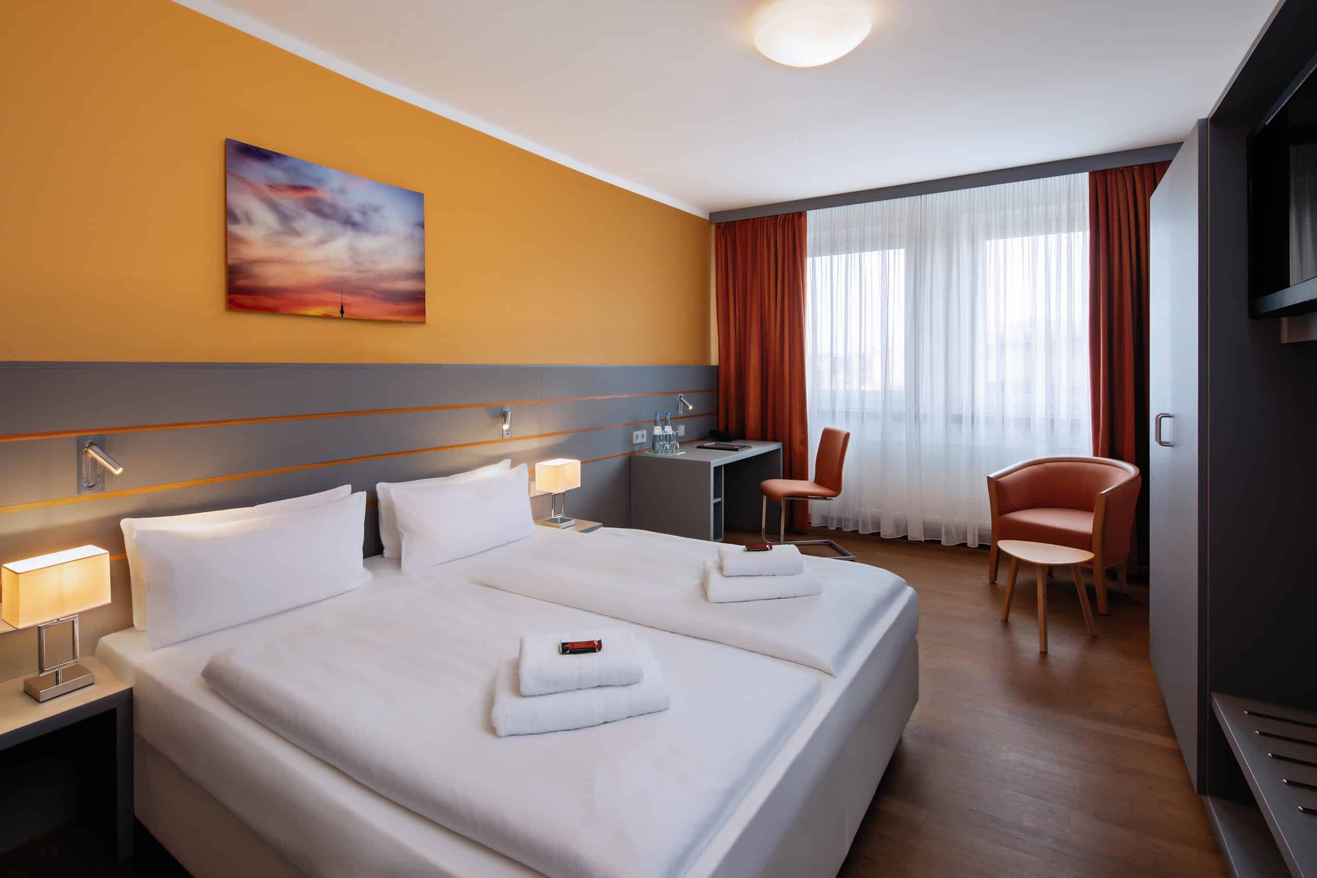 Doppelzimmer mit zwei Betten, einem Schreibtisch und einem Stuhl in einem modernen Hotelzimmer.