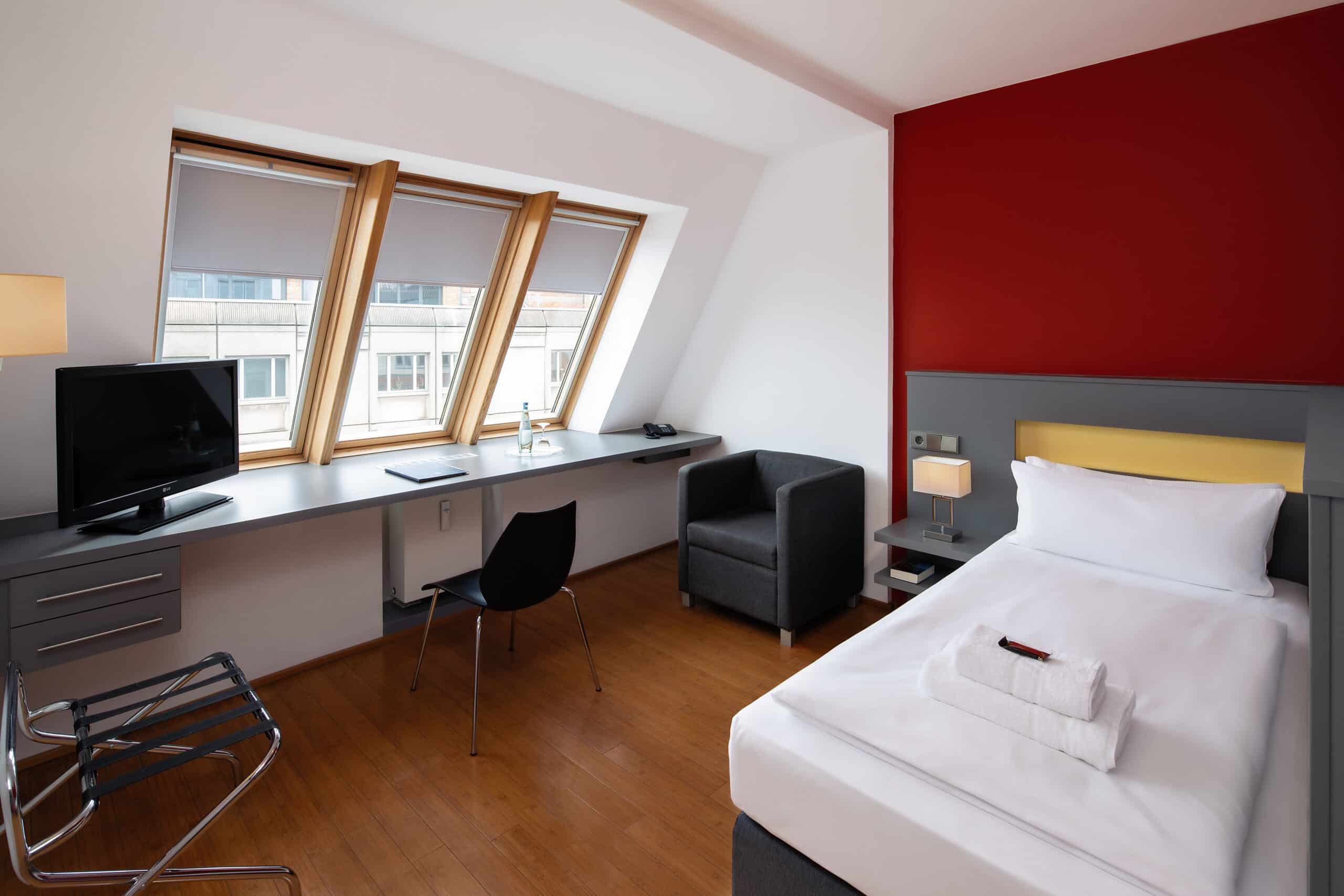 Einzelzimmer mit einem Bett, Schreibtisch, Stuhl und Fernseher im Hotel Dietrich Bonhoeffer Haus.
