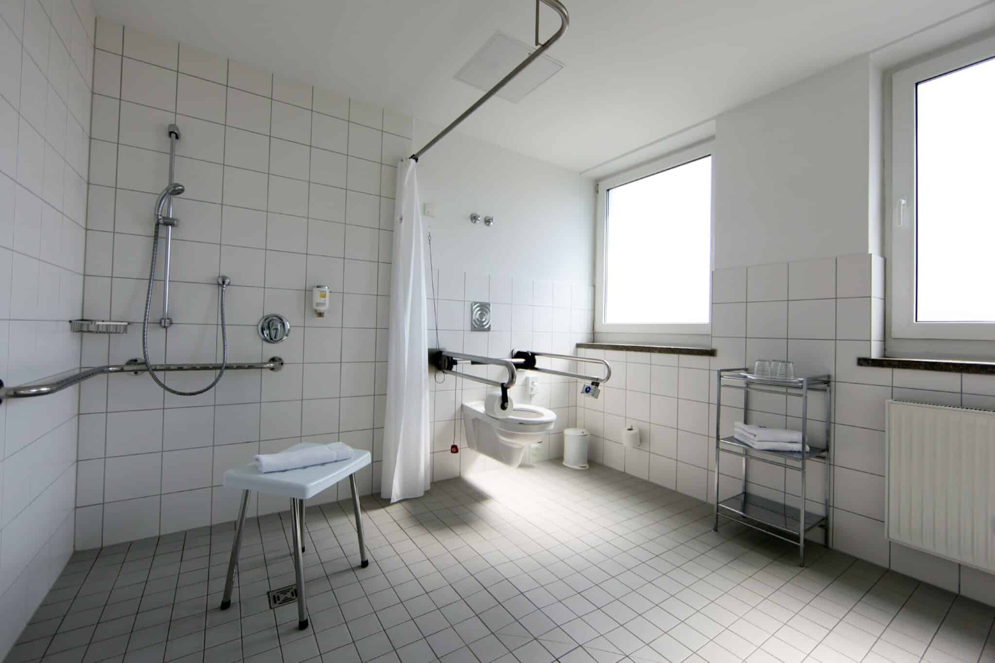 Barrierefreies Badezimmer mit Dusche, Haltegriffen und Toilettenstuhl im Hotel Dietrich Bonhoeffer Haus.