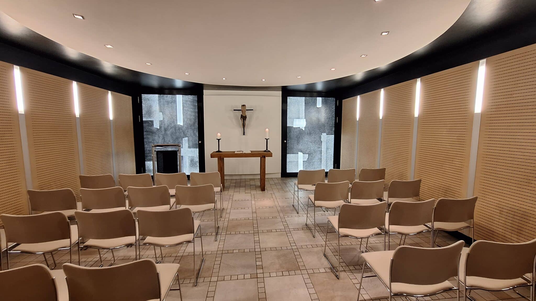 Innenansicht einer Kapelle mit einem Kreuz, einem Tisch und Stühlen in einem modernen Design.