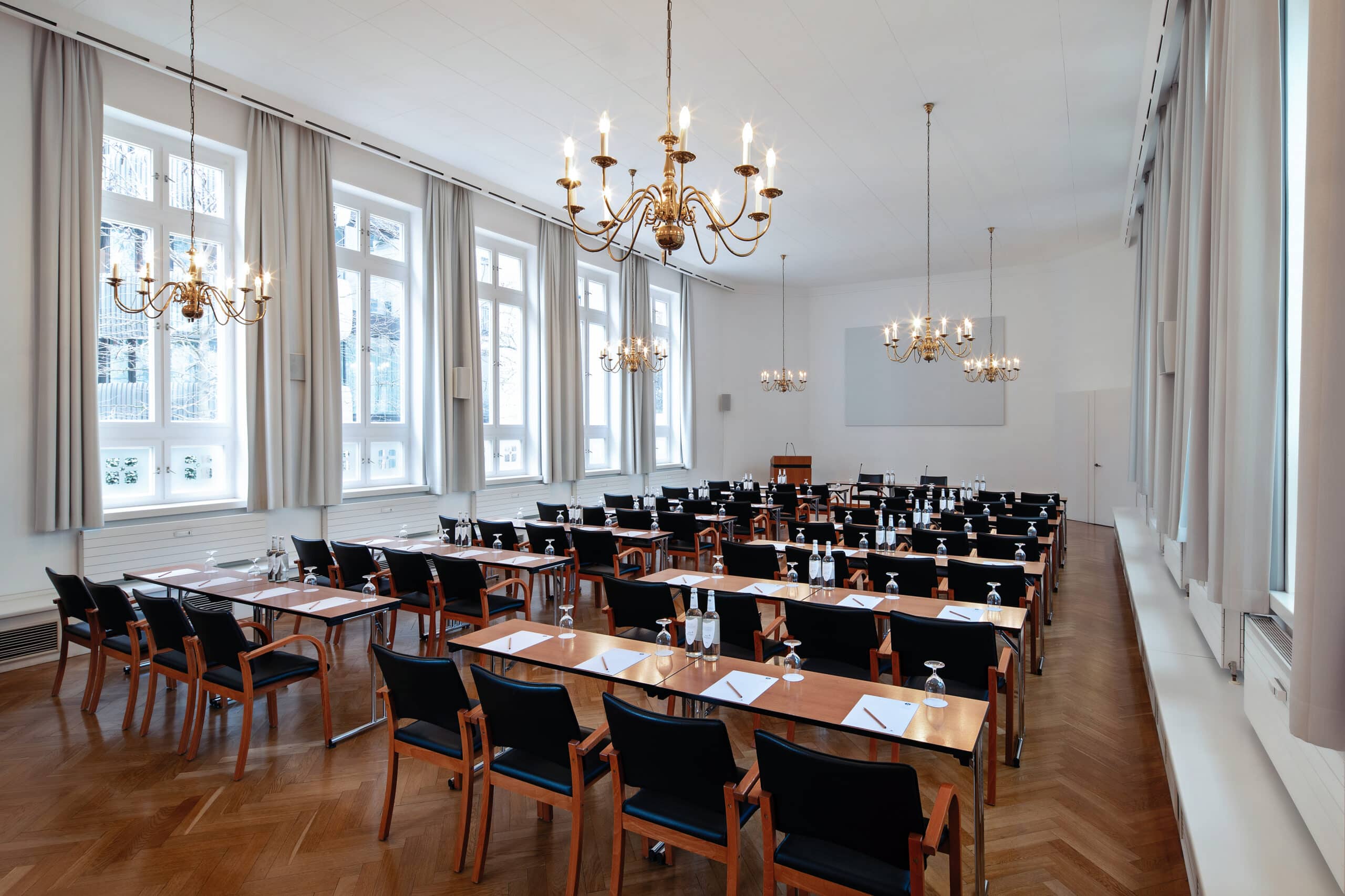 Konferenzraum mit Tischen und Stühlen, ausgestattet mit Kronleuchtern und Fenstern für Tageslicht.