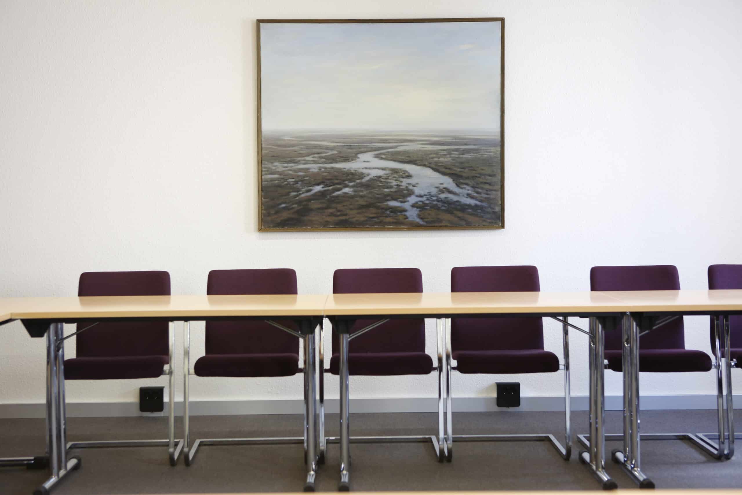 Konferenzraum mit einem langen Tisch und lila Stühlen, im Hintergrund ein Landschaftsgemälde.
