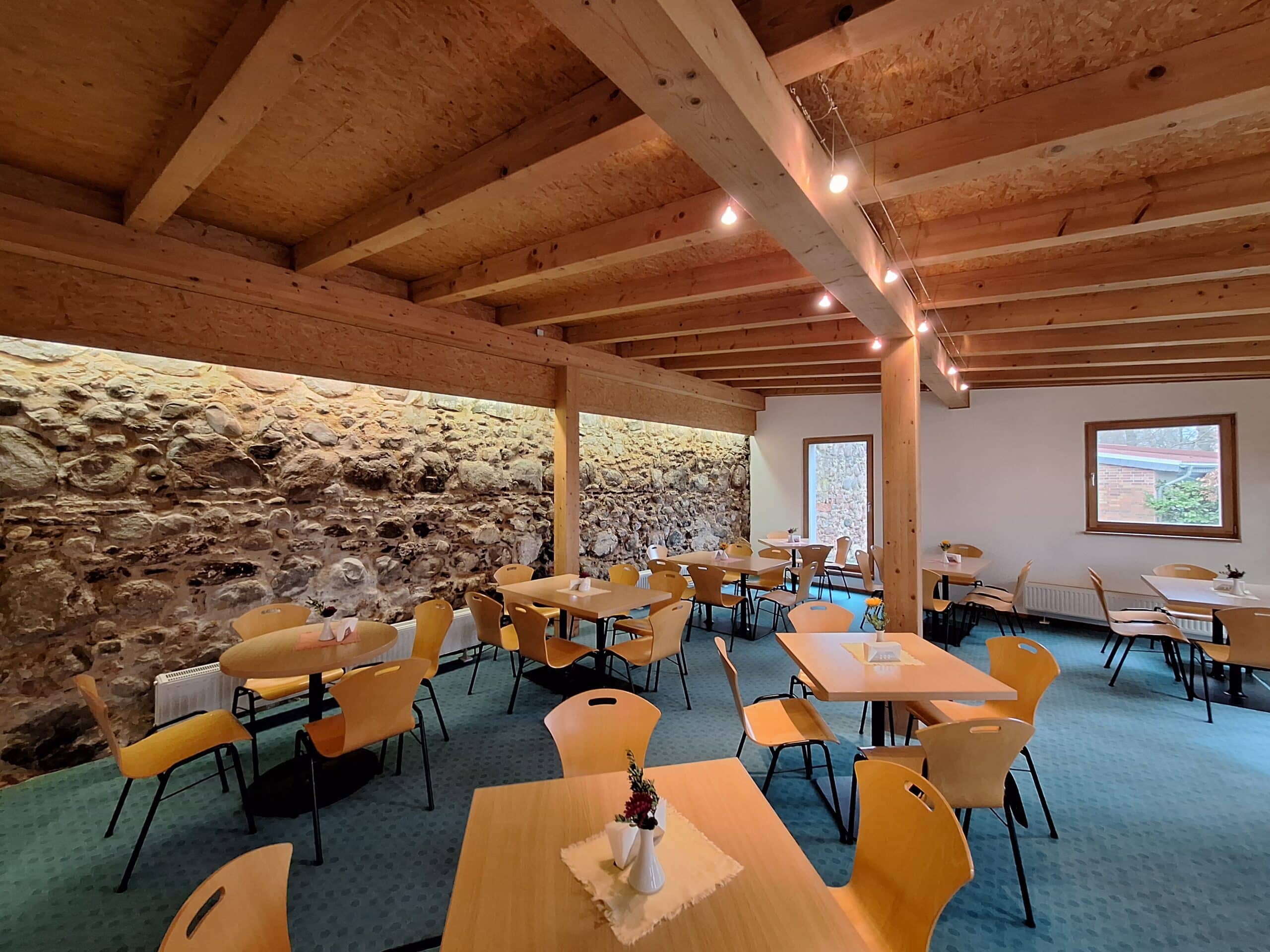 Innenansicht eines Seminarraums mit mehreren Tischen und Stühlen aus Holz in einem hellen Raum.