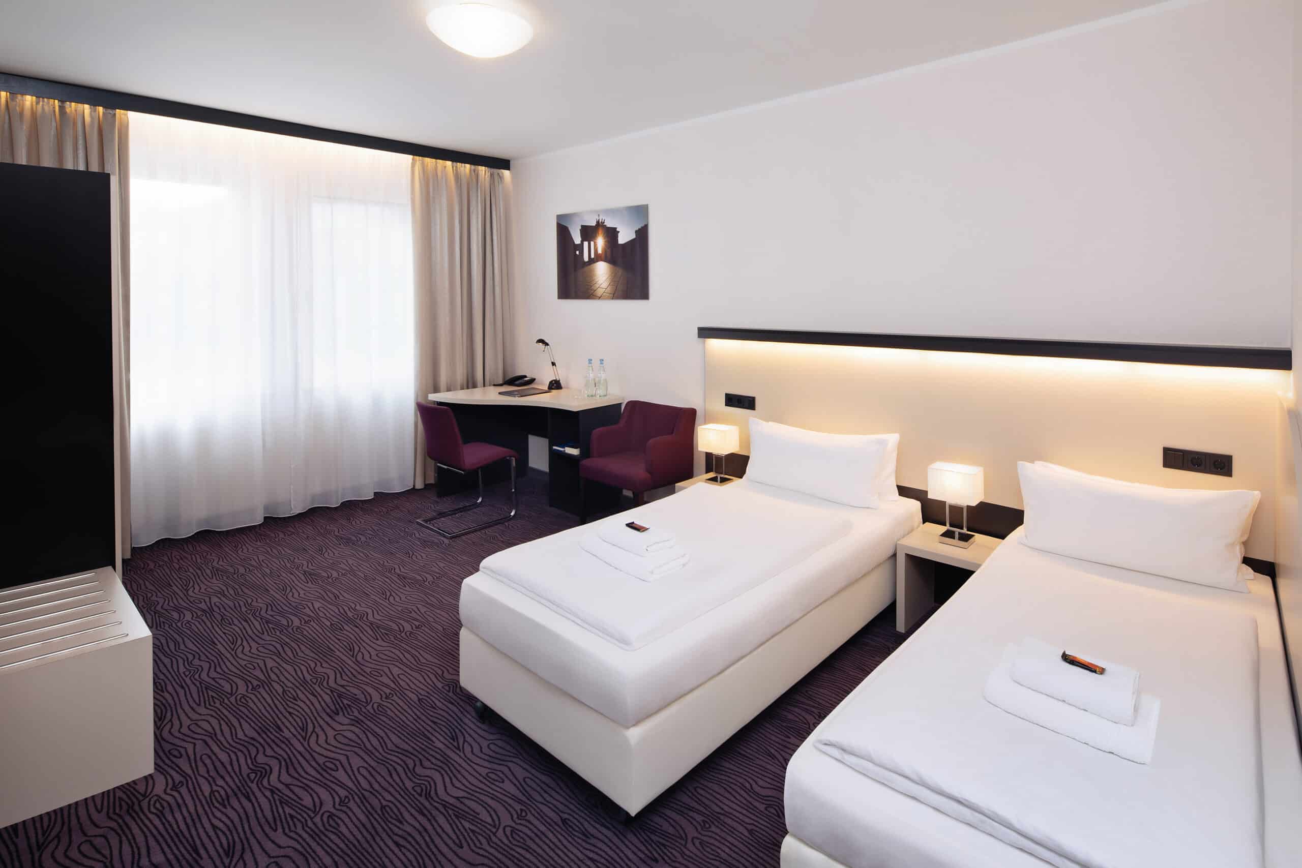 Zwei Einzelbetten in einem modernen Hotelzimmer mit minimalistischer Einrichtung und neutralen Farben.