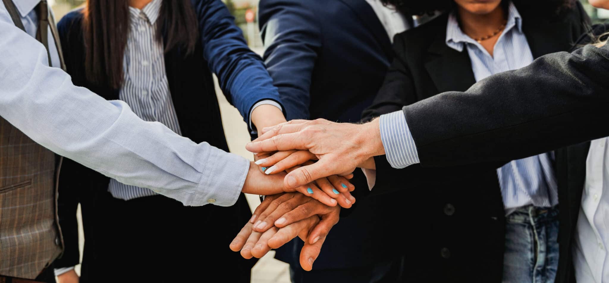 Hände von mehreren Personen, die übereinander gestapelt sind, symbolisieren Teamarbeit und Zusammenarbeit im Freien.