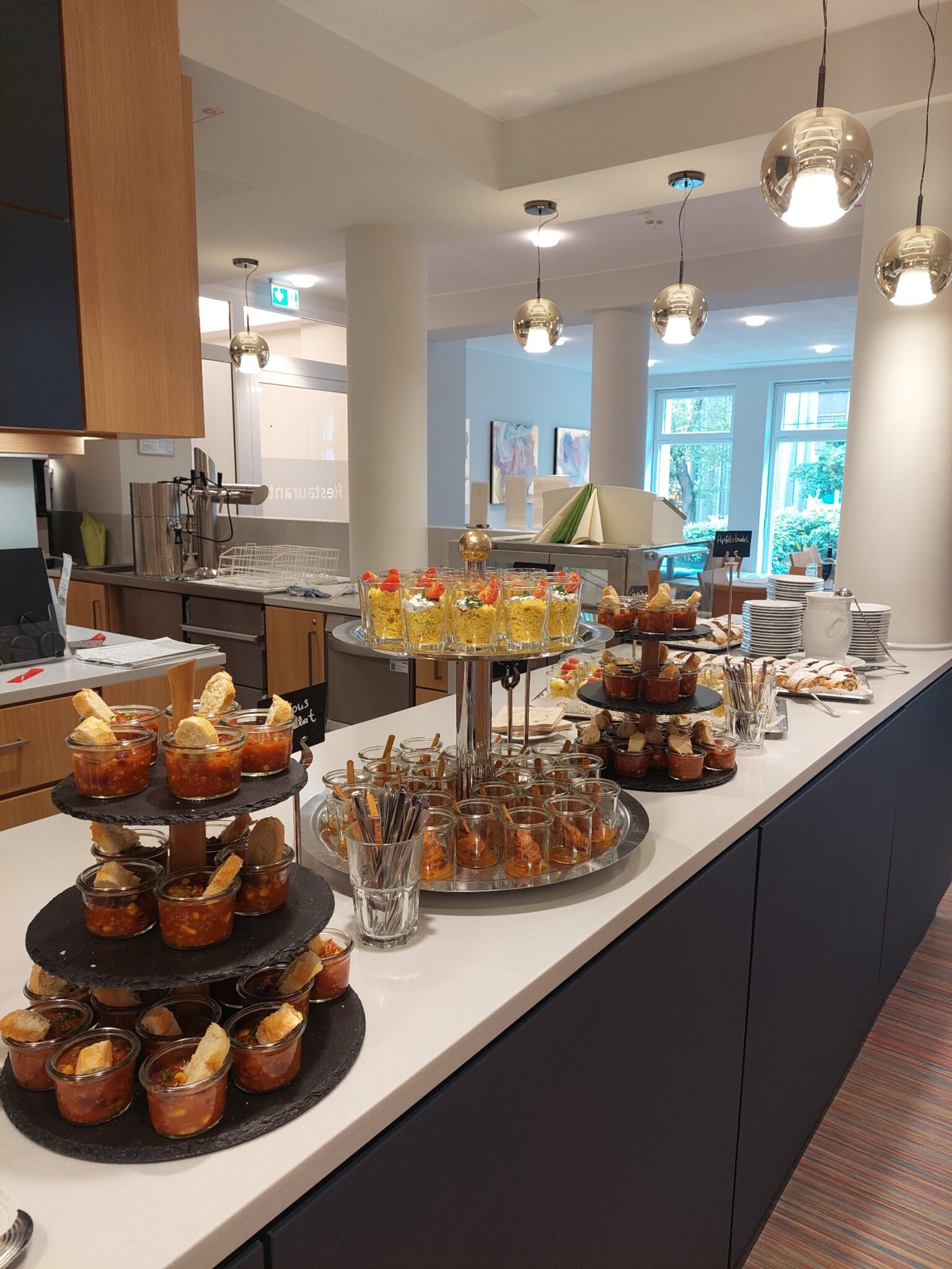 Buffet mit verschiedenen Desserts in Gläsern und auf einem Servierwagen im Restaurantbereich.