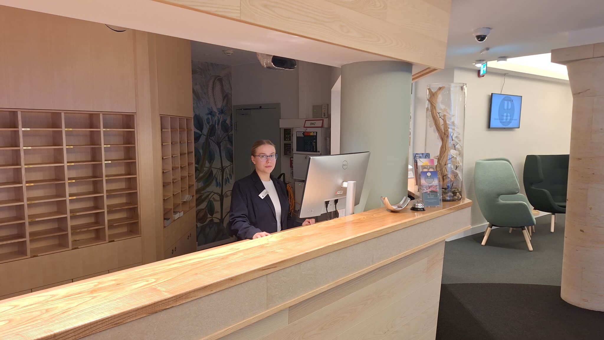 Rezeptionistin an einem Empfangstresen in einem modernen Hotel mit Computer und Holzoberfläche.